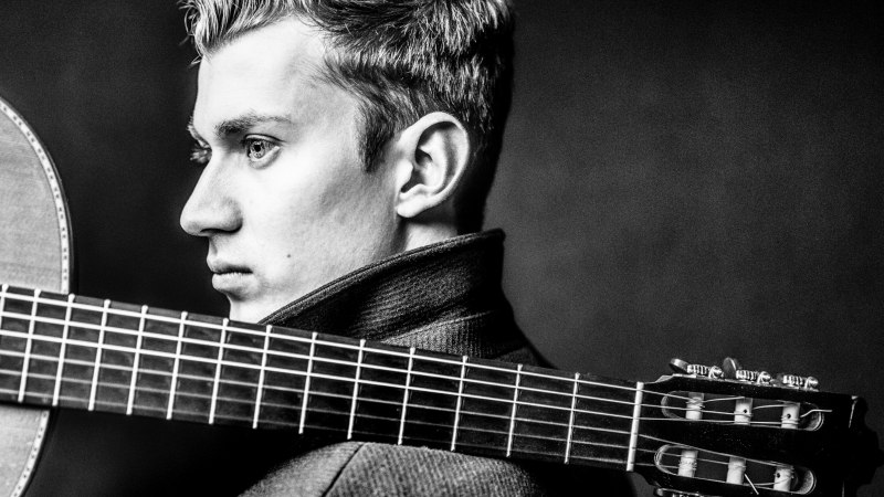 Schwarz-weiß Porträt eines Mannes mit Gitarre über der Schulter, im Profil. Er trägt einen hochgeschlossenen Mantel., © Marco Borggreve Schwarz-weiß Porträt eines Mannes mit Gitarre über der Schulter, im Profil. Er trägt einen hochgeschlossenen Mantel., © Marco Borggreve