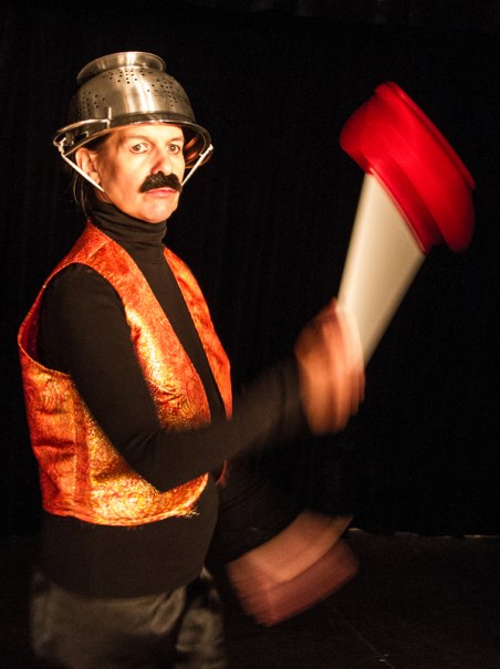 Eine Person in einem kreativen Theaterkost&uuml;m mit einem Sieb als Helm und einem roten Requisit in der Hand, vor schwarzem Hintergrund., &copy; Galli Theater Backnang