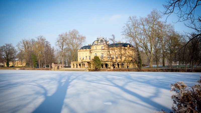 Seeschloss Monrepos im Winter, umgeben von kahlen Bäumen. Der See ist gefroren, und die Schatten der Bäume erstrecken sich über das Eis., © Tourismus & Events Ludwigsburg, Benjamin Stollenberg