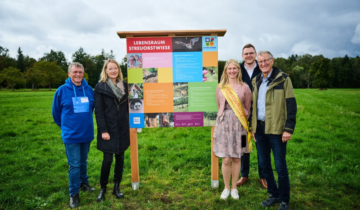 F&uuml;nf Personen posieren vor einem bunten Informationsschild mit der Aufschrift 'Lebensraum Streuobstwiese' auf einer gr&uuml;nen Wiese., &copy; Natur.Nah. Sch&ouml;nbuch & Heckeng&auml;u