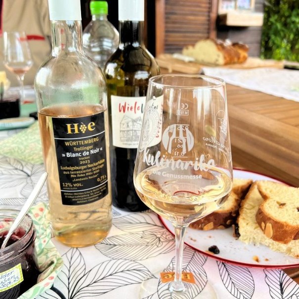 Zwei Weinflaschen und ein Glas Wei&szlig;wein stehen auf einem Tisch mit Geb&auml;ck. Im Hintergrund sind weitere Getr&auml;nke und ein Holzbrett zu sehen., &copy; Quelle: Manuela Priber; Tourismus & Events Ludwigsburg