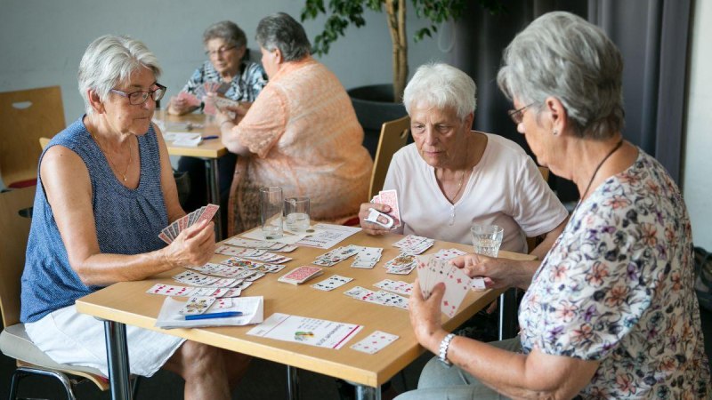Drei ältere Frauen spielen Karten an einem Tisch, während im Hintergrund zwei weitere Frauen ebenfalls Karten spielen., © �Roberto Bulgrin Drei ältere Frauen spielen Karten an einem Tisch, während im Hintergrund zwei weitere Frauen ebenfalls Karten spielen., © �Roberto Bulgrin