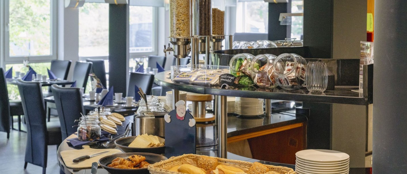 Ein Frühstücksbuffet mit Brötchen, Croissants, Müsli und Marmelade in einem hellen Speiseraum mit gedeckten Tischen., © Plaza INN Stuttgart-Filderstadt Ein Frühstücksbuffet mit Brötchen, Croissants, Müsli und Marmelade in einem hellen Speiseraum mit gedeckten Tischen., © Plaza INN Stuttgart-Filderstadt