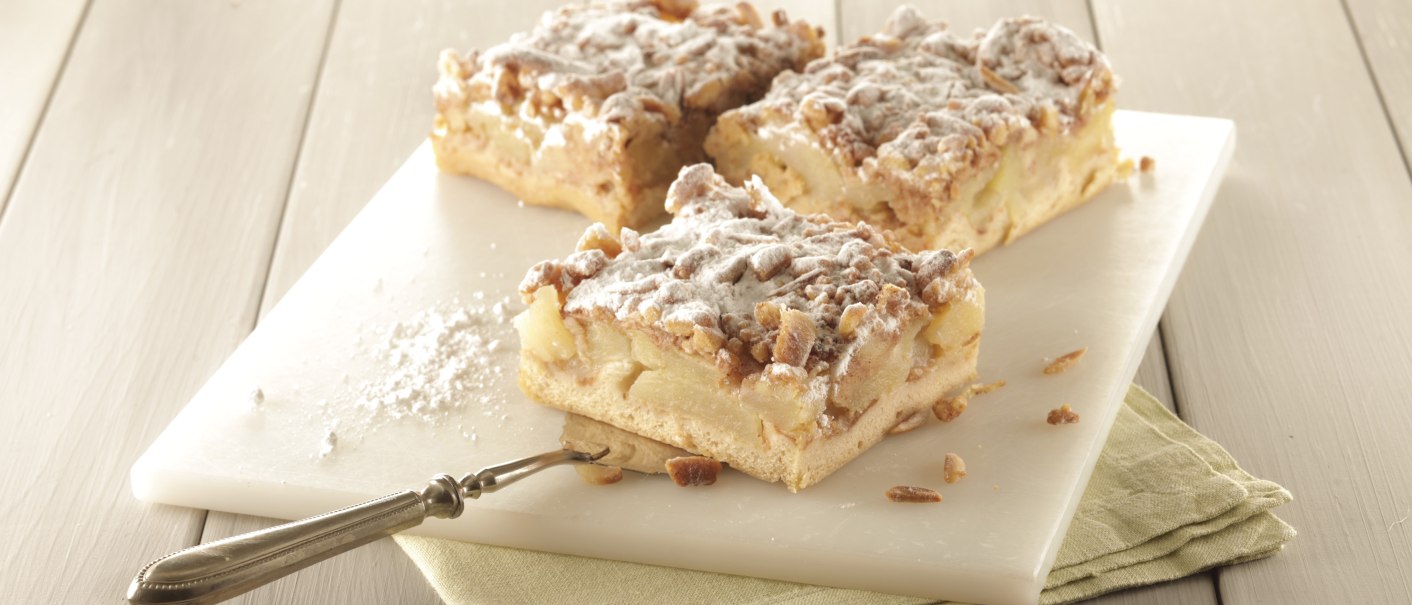 Drei Apfelschnitten mit Streuseln und Puderzucker auf einem weißen Brett, daneben ein Messer auf einem grünen Tuch., © Bäckerei Veit, Victoria Huber Drei Apfelschnitten mit Streuseln und Puderzucker auf einem weißen Brett, daneben ein Messer auf einem grünen Tuch., © Bäckerei Veit, Victoria Huber