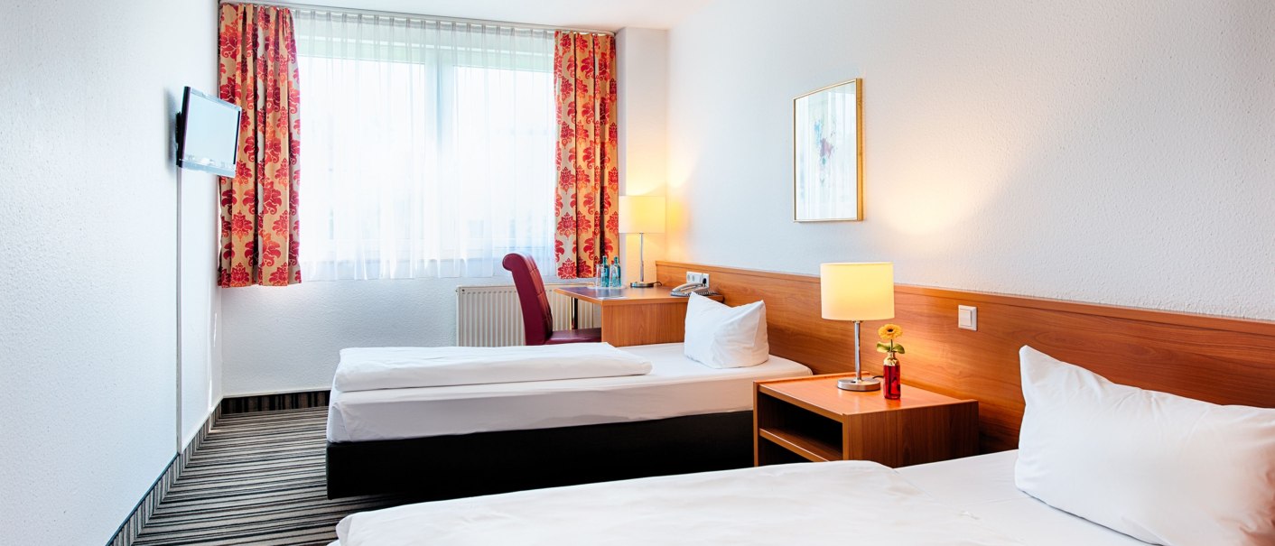 Helles Zweibettzimmer mit zwei Einzelbetten, Nachttisch mit Lampe, Schreibtisch, Fernseher und roten Vorh&auml;ngen., &copy; ACHAT Hotels Deutschland