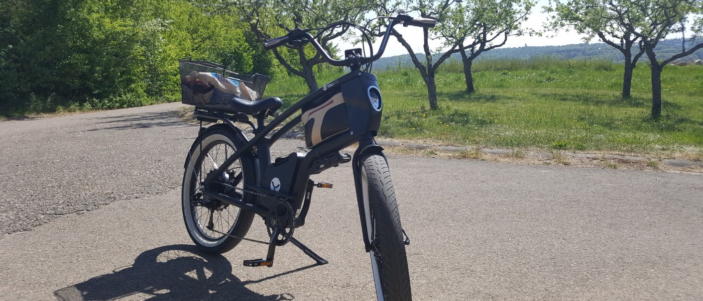 Ein schwarzes Youmo-E-Bike steht auf einer Straße in einer grünen, ländlichen Umgebung mit Bäumen im Hintergrund., © Hotel Weinstadt