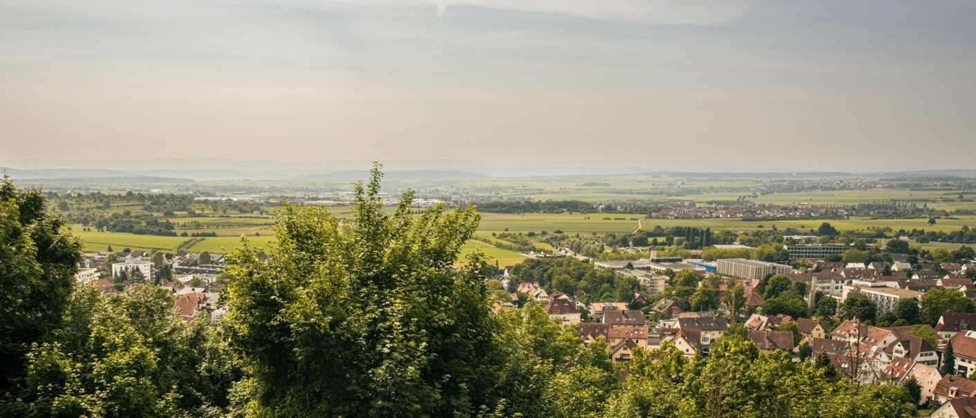 Panoramablick auf eine Stadt mit umliegenden Feldern und B&auml;umen, die sich bis zum Horizont erstrecken. Der Himmel ist klar und sonnig., &copy; Stuttgart-Marketing GmbH, Sarah Schmid