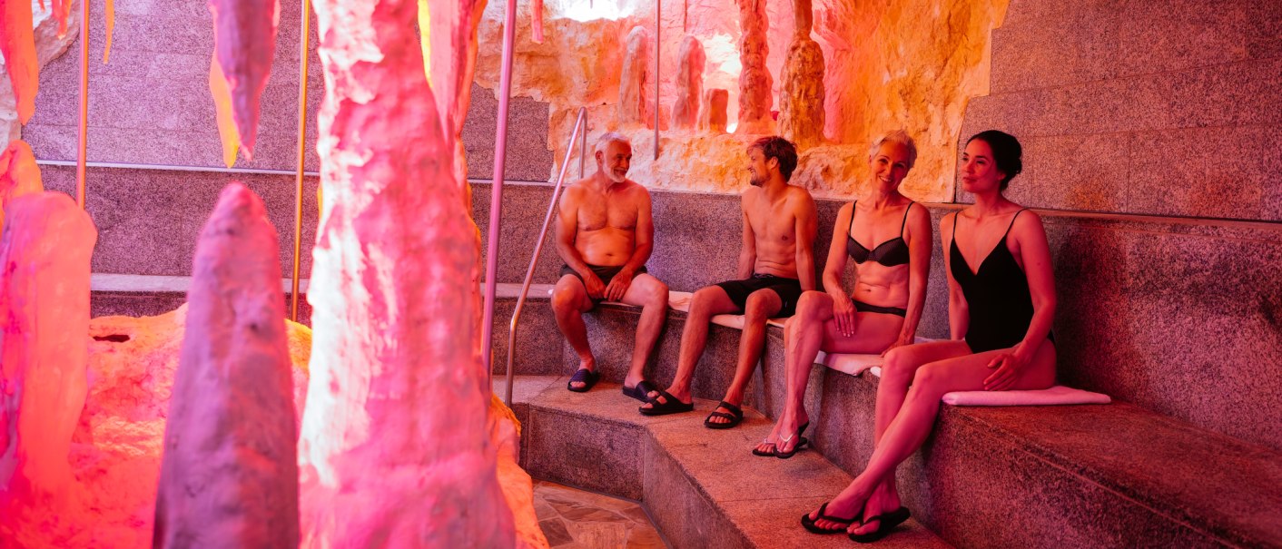Vier Personen sitzen in einer Therme mit rotem Licht und Felsformationen. Sie tragen Badebekleidung und wirken entspannt., &copy; Thomas Niederm&uuml;ller