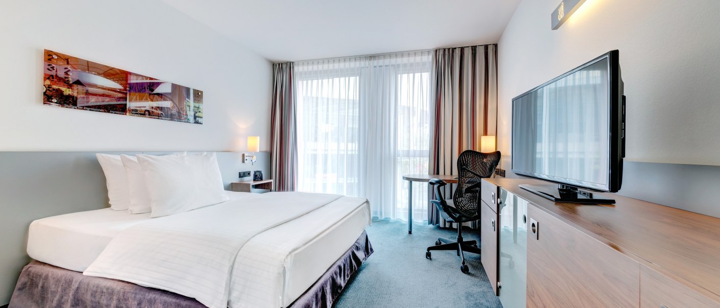Modernes Hotelzimmer mit Queensize-Bett, Schreibtisch, Stuhl und Flachbildfernseher. Große Fenster mit Vorhängen lassen viel Licht herein., © Hilton Garden Inn Stuttgart Neckarpark Modernes Hotelzimmer mit Queensize-Bett, Schreibtisch, Stuhl und Flachbildfernseher. Große Fenster mit Vorhängen lassen viel Licht herein., © Hilton Garden Inn Stuttgart Neckarpark