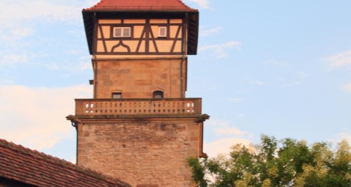 Ein historischer Wachturm mit Fachwerk und rotem Dach, umgeben von Bäumen und einer Steinmauer, vor einem blauen Himmel mit Wolken., © Waiblingen - Stuttgart-Marketing GmbH Ein historischer Wachturm mit Fachwerk und rotem Dach, umgeben von Bäumen und einer Steinmauer, vor einem blauen Himmel mit Wolken., © Waiblingen - Stuttgart-Marketing GmbH
