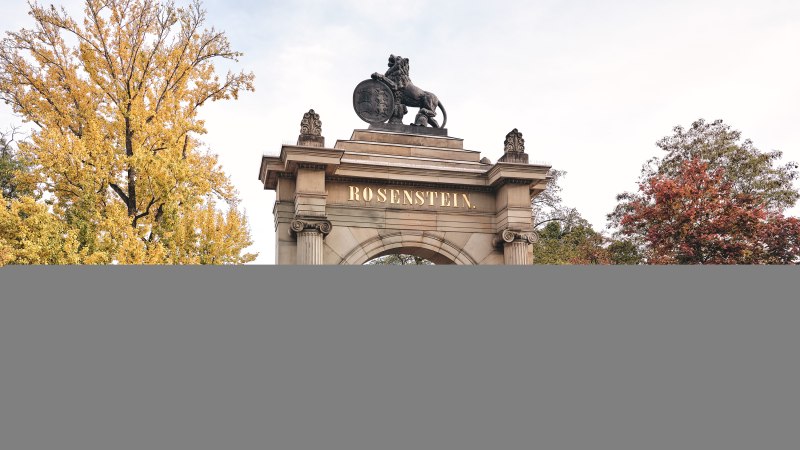 Historisches Tor mit 'Rosenstein'-Schriftzug, flankiert von Gebäuden. Herbstliche Bäume im Hintergrund, zwei Personen spazieren., © Stuttgart-Marketing GmbH, Christoph Düpper
