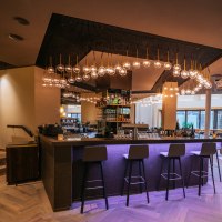 Moderne Bar mit stilvoller Beleuchtung, hohen St&uuml;hlen und gem&uuml;tlichen Sitzbereichen. Die Atmosph&auml;re ist einladend und elegant., &copy; Breuninger