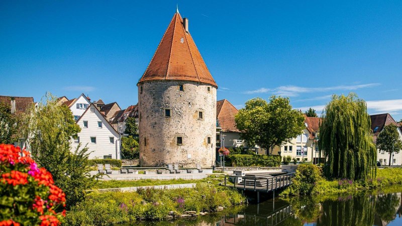 Der historische Pulverturm in Vaihingen an der Enz, umgeben von malerischen Häusern und einem ruhigen Fluss unter blauem Himmel., © SMG, Sarah Schmid Der historische Pulverturm in Vaihingen an der Enz, umgeben von malerischen Häusern und einem ruhigen Fluss unter blauem Himmel., © SMG, Sarah Schmid