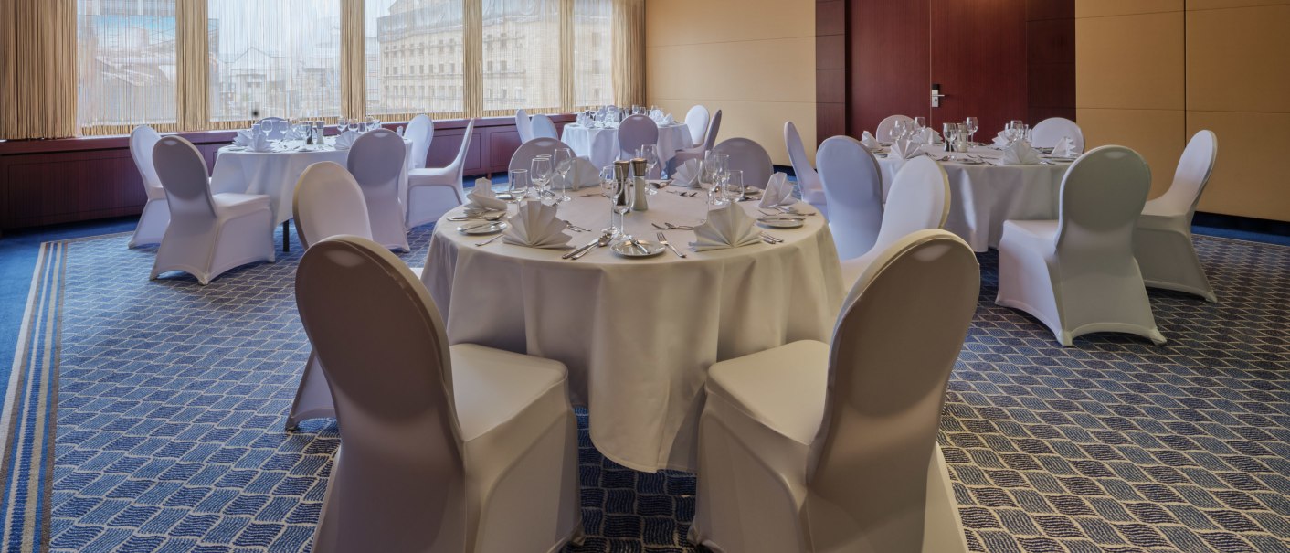 Eleganter Bankettsaal mit runden, festlich gedeckten Tischen und weißen Stuhlhussen, großer Kronleuchter an der Decke., © Steigenberger Graf Zeppelin