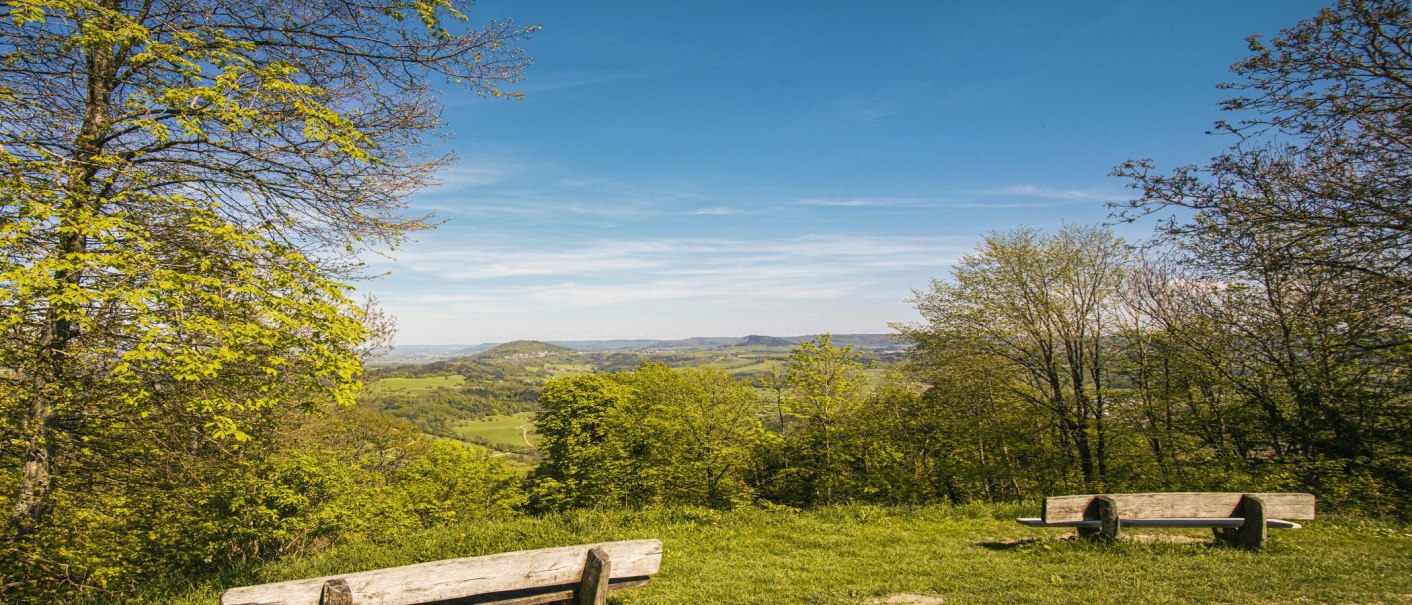 Aussicht vom Hohenstaufen mit zwei Holzbänken im Vordergrund, umgeben von grünen Bäumen und einem weiten Blick über die Landschaft., © SMG, Sarah Schmid Aussicht vom Hohenstaufen mit zwei Holzbänken im Vordergrund, umgeben von grünen Bäumen und einem weiten Blick über die Landschaft., © SMG, Sarah Schmid