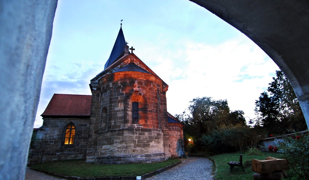 Die Stiftskirche Faurndau bei Dämmerung, umgeben von Bäumen und einem Kiesweg. Der Himmel ist leicht bewölkt., © Stadtmarketing Göppingen Die Stiftskirche Faurndau bei Dämmerung, umgeben von Bäumen und einem Kiesweg. Der Himmel ist leicht bewölkt., © Stadtmarketing Göppingen