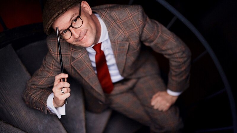 Mann in kariertem Anzug und roter Krawatte auf einer Wendeltreppe, hält einen Zauberstab., © Kulturhaus Schwanen