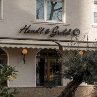 Das Bild zeigt die Fassade des Restaurants Hendl & Gretel mit einem Sonnenschirm und Pflanzen im Vordergrund., &copy; SMG, Sarah Schmid