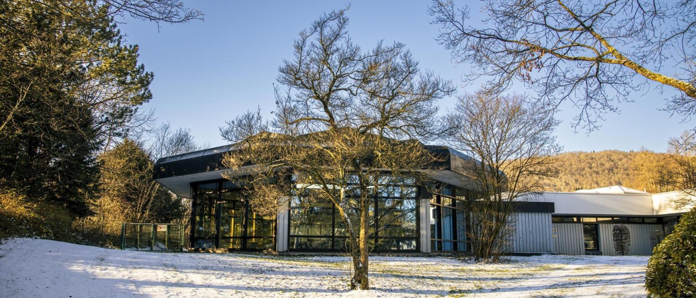 Moderne Therme in winterlicher Landschaft, umgeben von kahlen Bäumen und leichtem Schneefall. Klare Glasfassaden reflektieren die Umgebung., © Stuttgart-Marketing GmbH, Sarah Schmid Moderne Therme in winterlicher Landschaft, umgeben von kahlen Bäumen und leichtem Schneefall. Klare Glasfassaden reflektieren die Umgebung., © Stuttgart-Marketing GmbH, Sarah Schmid