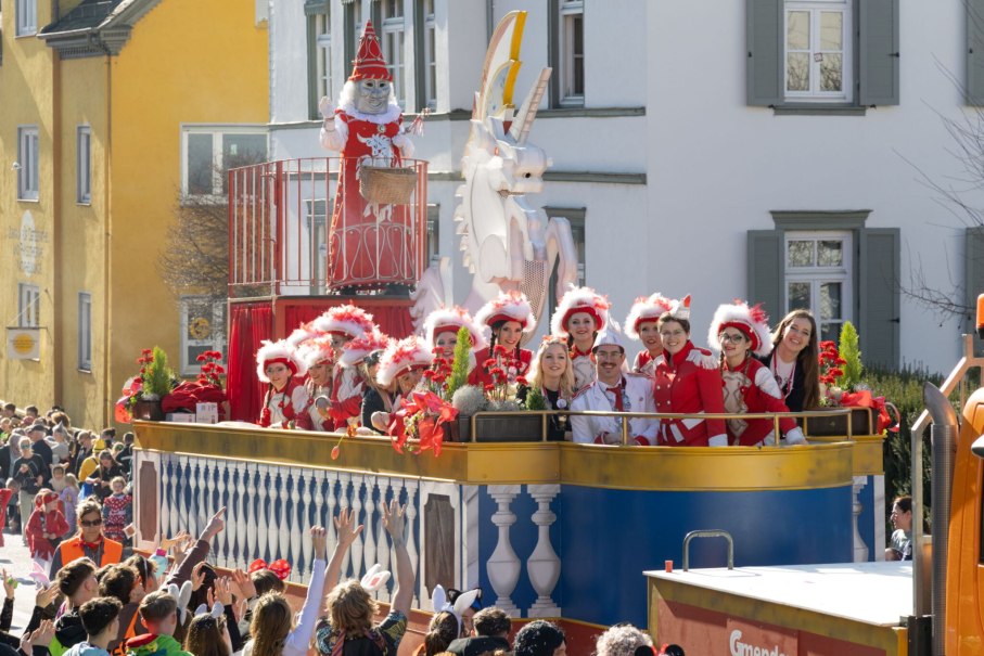 Ein festlich geschm&uuml;ckter Karnevalswagen mit verkleideten Menschen in roten Kost&uuml;men zieht durch eine belebte Stra&szlig;e. Zuschauer jubeln und winken., &copy; F&uuml;r die Bildrechte: Amt f&uuml;r Medien und Kommunikation Schw&auml;bisch Gm&uuml;nd