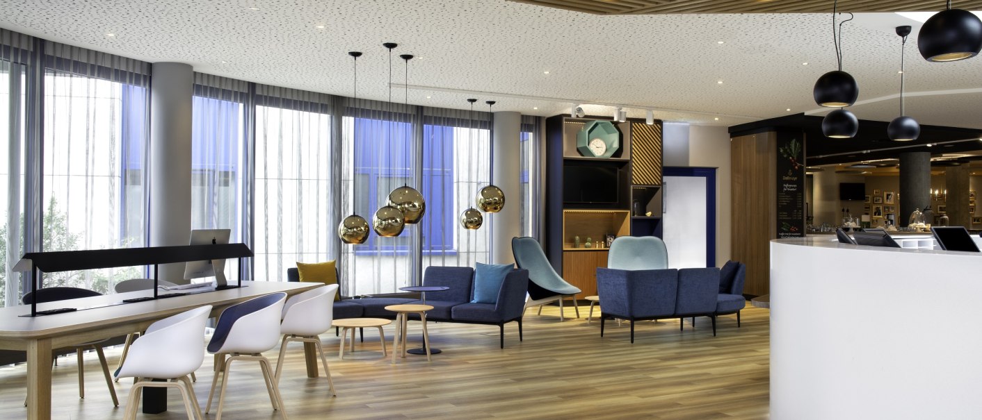 Moderne Lobby mit Holzdecke, blauen und weißen Möbeln, dekorativen Lampen und einem Empfangstresen., © Holiday Inn Moderne Lobby mit Holzdecke, blauen und weißen Möbeln, dekorativen Lampen und einem Empfangstresen., © Holiday Inn