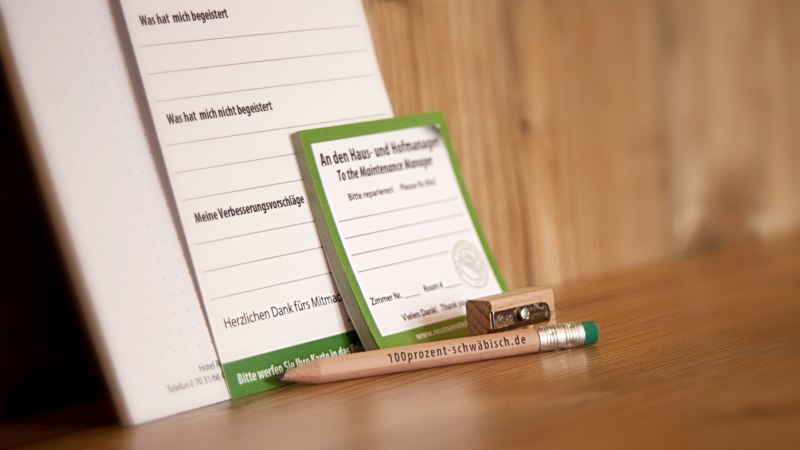 Ein Bleistift mit der Aufschrift "100prozent-schw&auml;bisch.de", ein Anspitzer und Formulare f&uuml;r Meinungen und Reparaturanfragen auf einem Holztisch., &copy; TOMAS