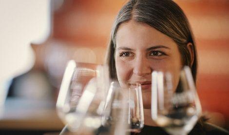 Eine Frau sitzt in einer Vinothek und schaut l&auml;chelnd durch mehrere Weingl&auml;ser. Die Atmosph&auml;re wirkt entspannt und einladend., &copy; TeamWerk Esslingen