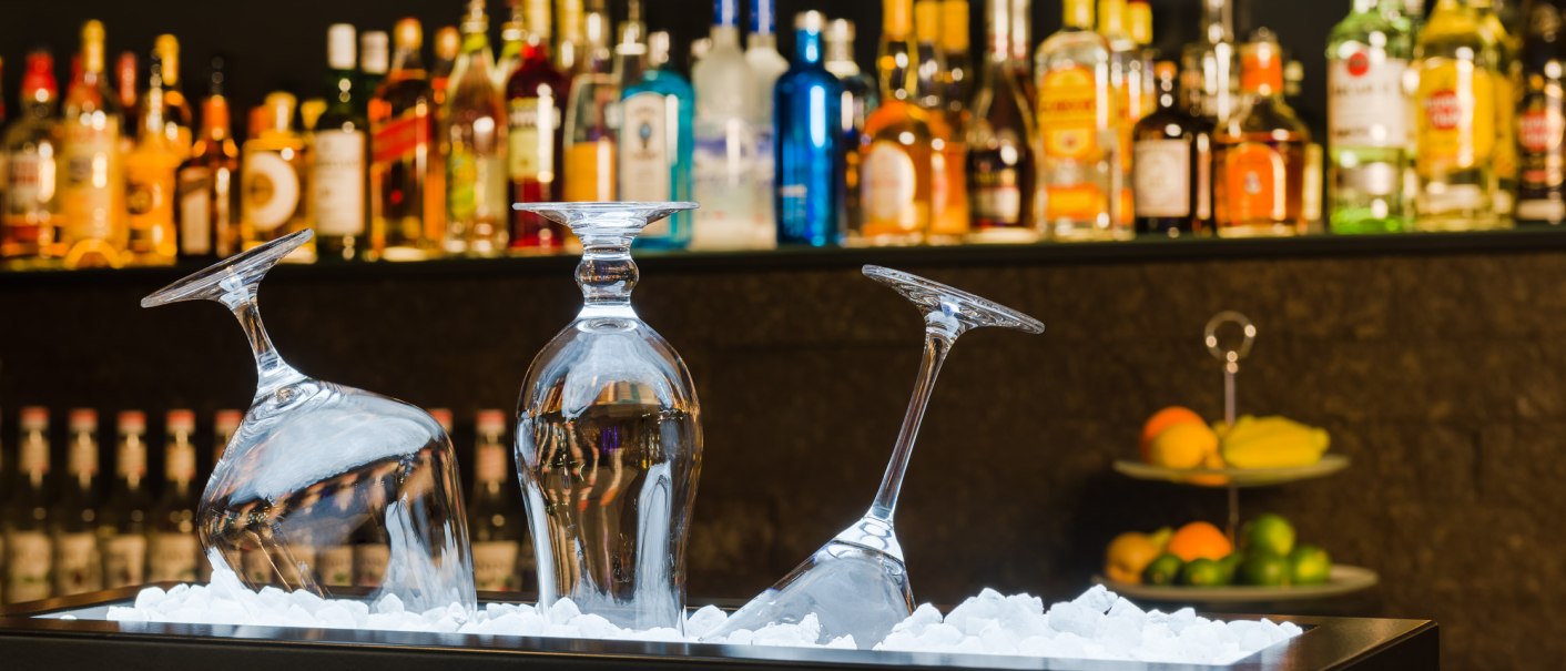 Drei umgedrehte Gläser auf Eis vor einer Bar. Im Hintergrund sind zahlreiche bunte Flaschen zu sehen. Rechts steht eine Etagere mit Obst., © MASEVEN Stuttgart SI-Centrum Drei umgedrehte Gläser auf Eis vor einer Bar. Im Hintergrund sind zahlreiche bunte Flaschen zu sehen. Rechts steht eine Etagere mit Obst., © MASEVEN Stuttgart SI-Centrum