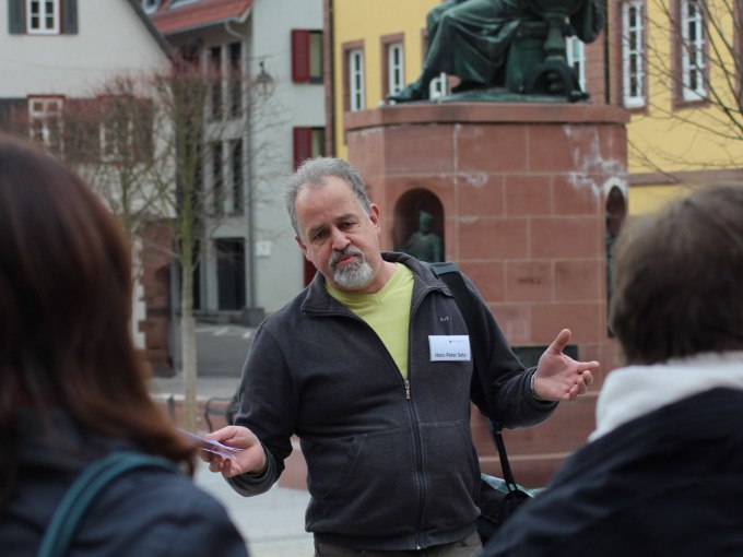 Ein Mann spricht zu einer Gruppe von Menschen auf einem Platz. Im Hintergrund ist eine Statue zu sehen. Die Szene wirkt wie eine Stadtf&uuml;hrung., &copy; Stadtverwaltung Weil der Stadt