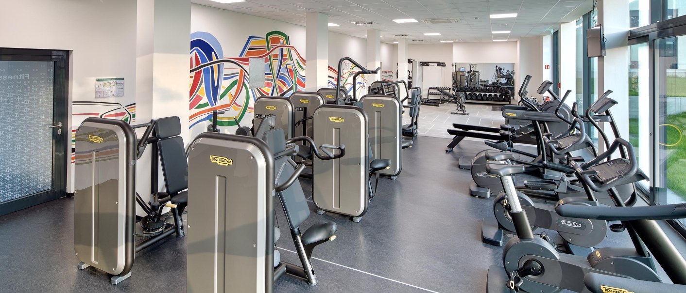 Modernes Fitnessstudio mit verschiedenen Trainingsgeräten, bunter Wandkunst und großen Fenstern für viel Tageslicht., © Hotel am Remspark Modernes Fitnessstudio mit verschiedenen Trainingsgeräten, bunter Wandkunst und großen Fenstern für viel Tageslicht., © Hotel am Remspark