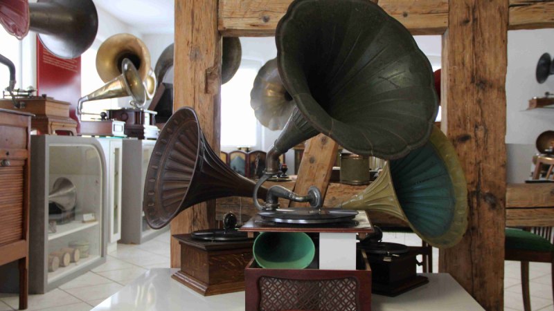 Antike Grammophone mit großen Trichtern in einem Raum mit Holzbalken und Vitrinen.