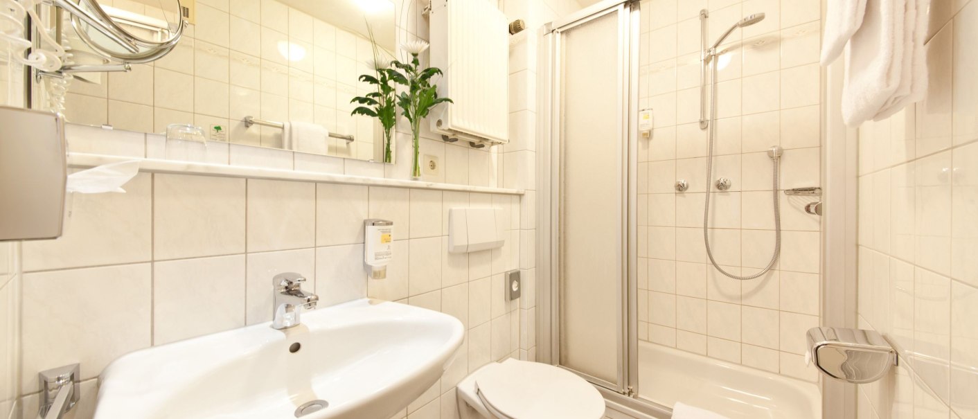 Helles, modernes Badezimmer mit Dusche, Waschbecken, Toilette und Handtuchhalter. Pflanzen und Spiegel ergänzen die Einrichtung., © Novum Boulevard Stuttgart City