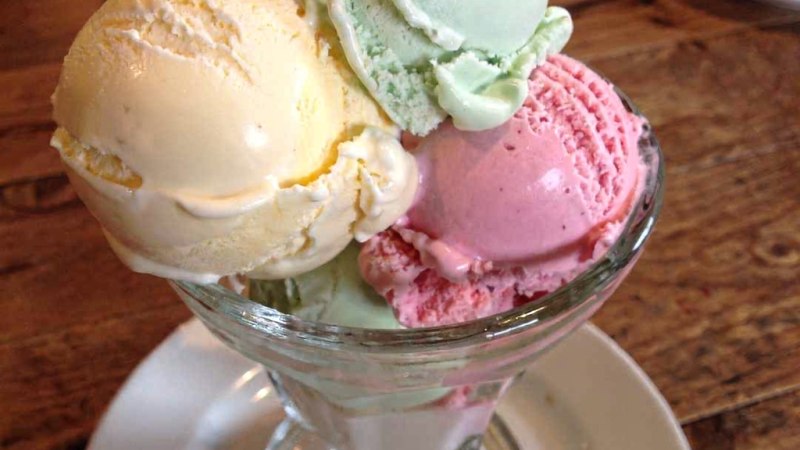 Ein Glasbecher mit drei Kugeln Eis in den Farben Gelb, Gr&uuml;n und Rosa steht auf einem Holztisch., &copy; StadtN&uuml;rtingen