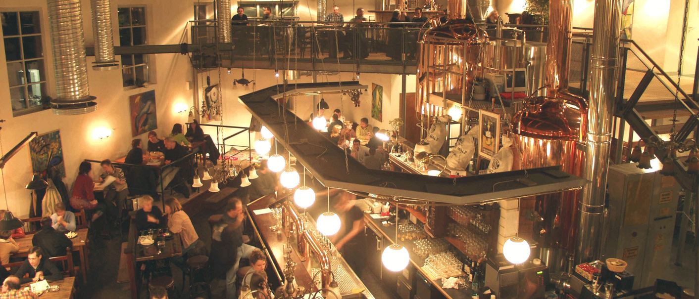 Belebtes Restaurant mit Braukesseln, Gästen an Tischen und einer Bar. Industrielles Design mit warmem Licht und moderner Einrichtung., © Kesselhaus, Schorndorf Belebtes Restaurant mit Braukesseln, Gästen an Tischen und einer Bar. Industrielles Design mit warmem Licht und moderner Einrichtung., © Kesselhaus, Schorndorf