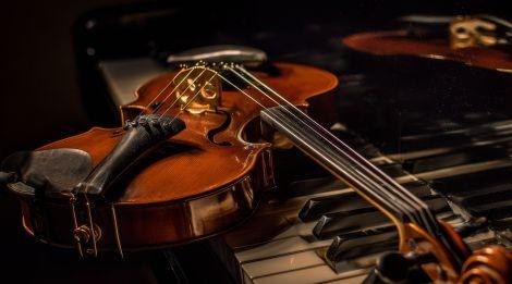 Eine Geige ruht auf den Tasten eines Klaviers, beleuchtet von warmem Licht, das die Holzmaserung betont., &copy; T&ouml;ne & Tannine. Foto: Teamwerk