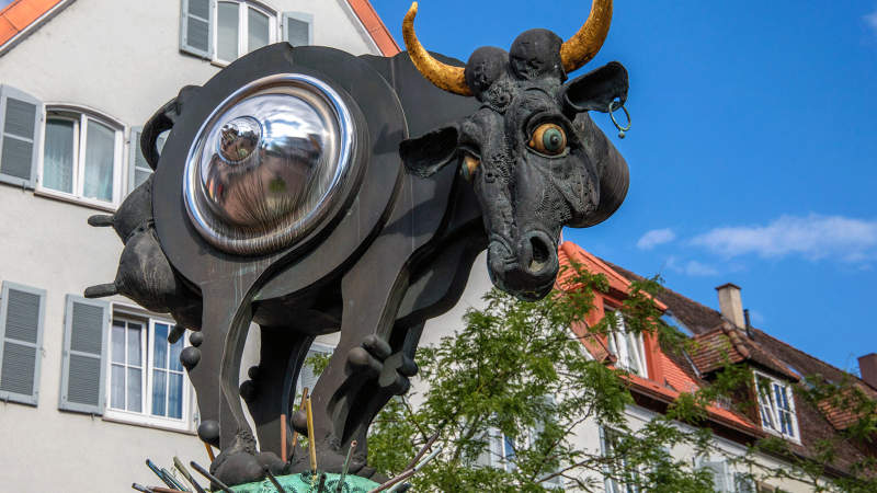 Surreale Kuhskulptur mit metallischem Bauch und goldenen Hörnern vor einem Gebäude mit roten Dachziegeln., © Stuttgart-Marketing GmbH Surreale Kuhskulptur mit metallischem Bauch und goldenen Hörnern vor einem Gebäude mit roten Dachziegeln., © Stuttgart-Marketing GmbH