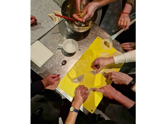 Teilnehmer eines Kochkurses formen gemeinsam Teigtaschen auf einem gelben Schneidebrett. Verschiedene Hände arbeiten zusammen., © Kultweine-Kochwelten-Kunstücke - Kochschule Sonja Lenz Teilnehmer eines Kochkurses formen gemeinsam Teigtaschen auf einem gelben Schneidebrett. Verschiedene Hände arbeiten zusammen., © Kultweine-Kochwelten-Kunstücke - Kochschule Sonja Lenz
