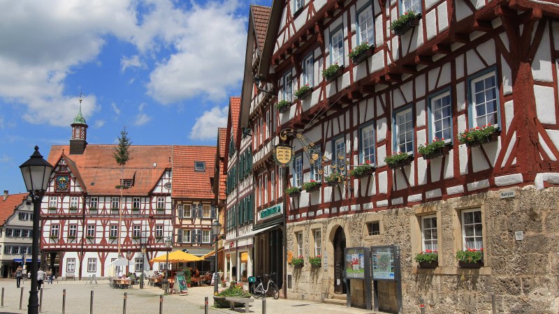 Fachwerkhäuser am Marktplatz von Bad Urach, blauer Himmel mit Wolken, Menschen sitzen draußen, Blumen schmücken die Fenster., © Armin Dieter Fachwerkhäuser am Marktplatz von Bad Urach, blauer Himmel mit Wolken, Menschen sitzen draußen, Blumen schmücken die Fenster., © Armin Dieter