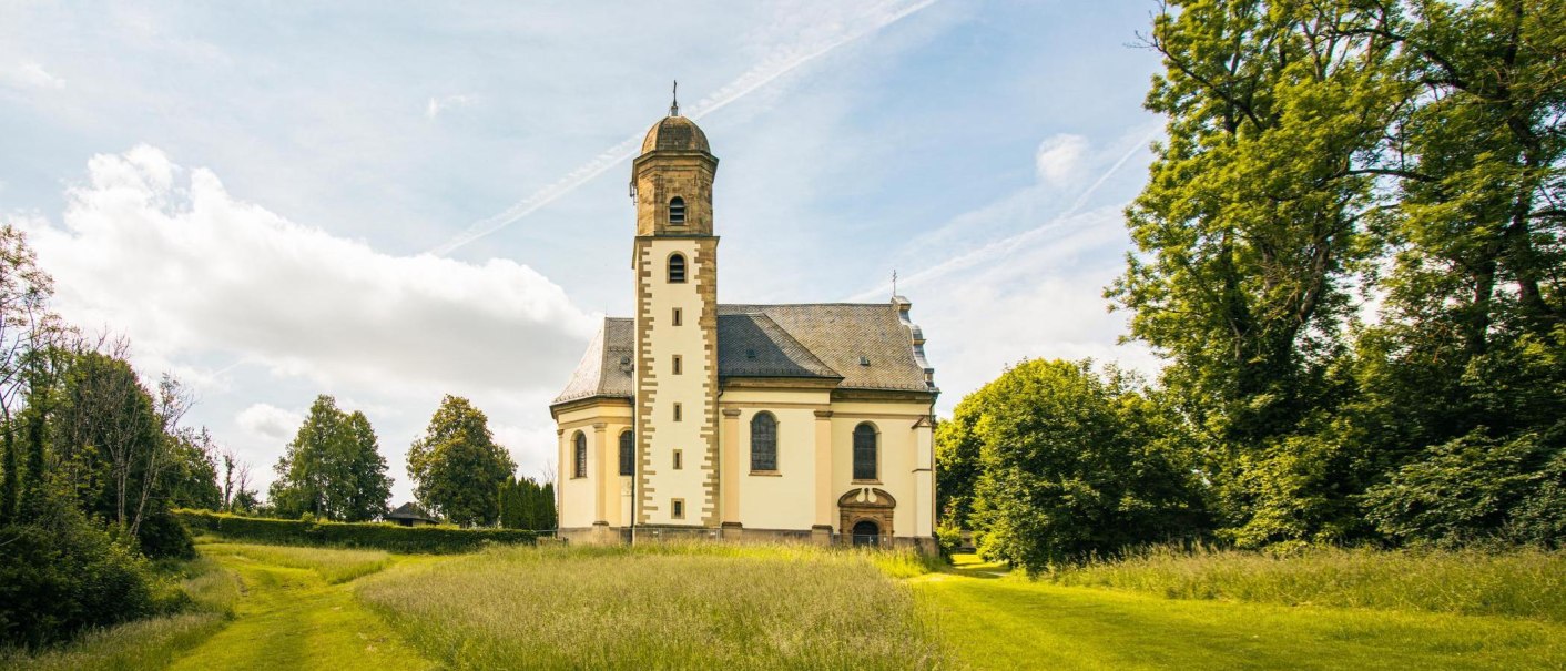 Die Barockkirche St. Maria auf dem Hohenrechberg steht malerisch inmitten einer grünen Wiese und Bäumen unter einem blauen Himmel., © SMG, Sarah Schmid Die Barockkirche St. Maria auf dem Hohenrechberg steht malerisch inmitten einer grünen Wiese und Bäumen unter einem blauen Himmel., © SMG, Sarah Schmid