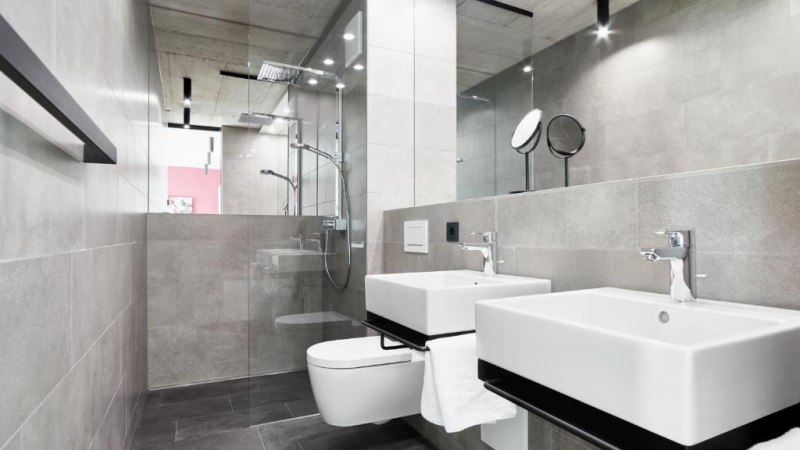 Modernes Badezimmer mit zwei Waschbecken, großer Spiegelwand, Regendusche und grauen Fliesen. Minimalistisches Design mit klaren Linien., © livisit bergapartments Modernes Badezimmer mit zwei Waschbecken, großer Spiegelwand, Regendusche und grauen Fliesen. Minimalistisches Design mit klaren Linien., © livisit bergapartments