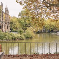 Ein Paar spaziert am Feuersee entlang, im Hintergrund die Johanneskirche und herbstliche Bäume. Ein Brunnen sprudelt im See., © SMG Christoph Düpper
