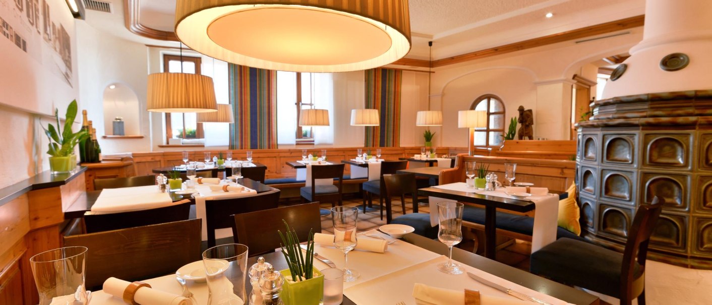 Elegantes Restaurant mit gedeckten Tischen, großen Lampen und einem Kachelofen. Die Einrichtung ist modern und einladend., © Ringhotel Adler Asperg