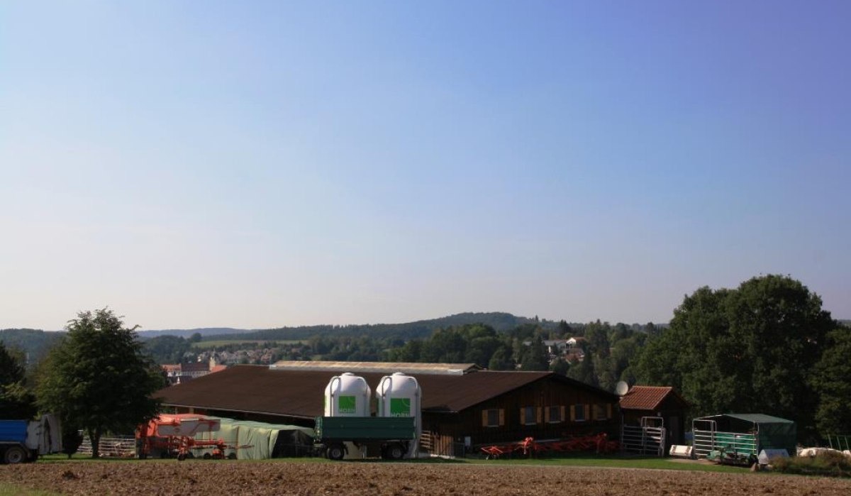 Ein Bauernhof mit Traktoren und landwirtschaftlichen Geräten, umgeben von Feldern und Bäumen unter einem klaren blauen Himmel., © Natur.Nah. Schönbuch & Heckengäu Ein Bauernhof mit Traktoren und landwirtschaftlichen Geräten, umgeben von Feldern und Bäumen unter einem klaren blauen Himmel., © Natur.Nah. Schönbuch & Heckengäu