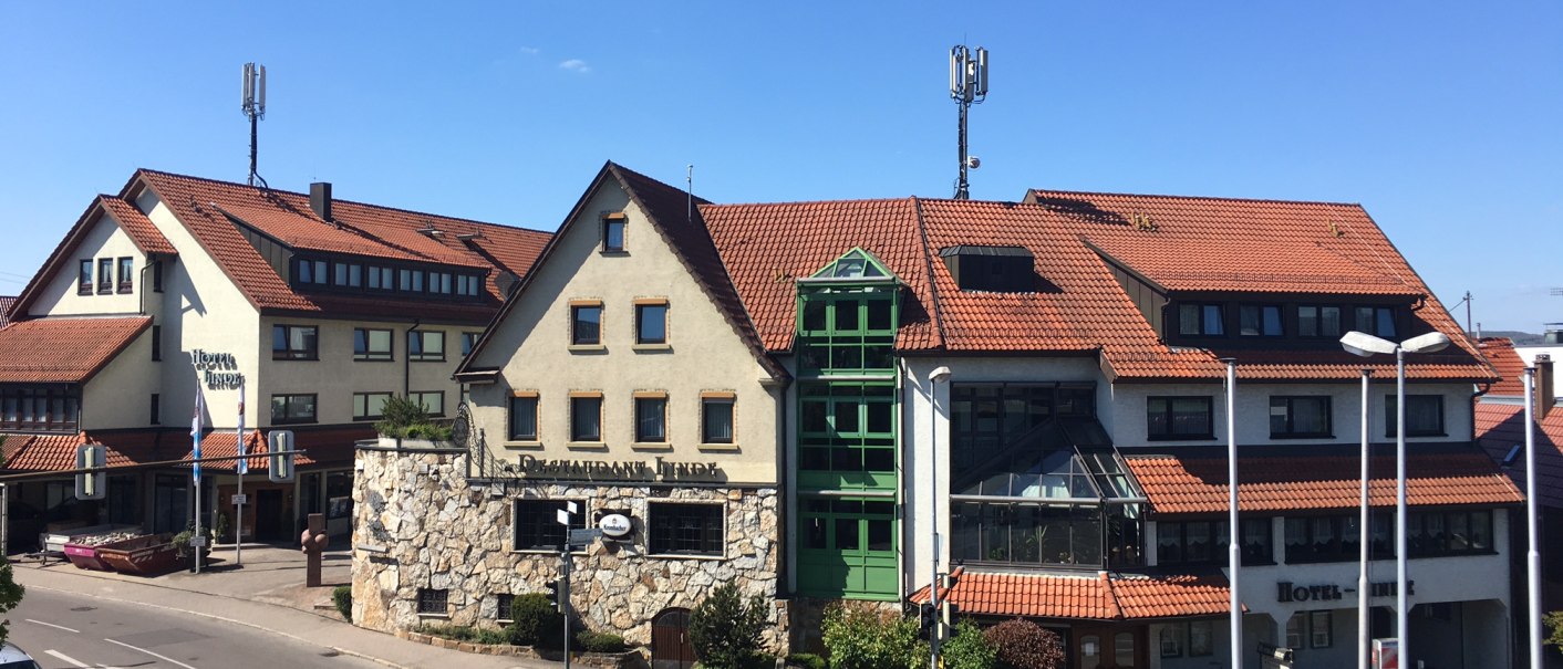 Das Neo Hotel Linde in Esslingen mit roten Ziegeldächern und grünen Fenstern, umgeben von einer Straße und unter blauem Himmel., © TOMAS Das Neo Hotel Linde in Esslingen mit roten Ziegeldächern und grünen Fenstern, umgeben von einer Straße und unter blauem Himmel., © TOMAS