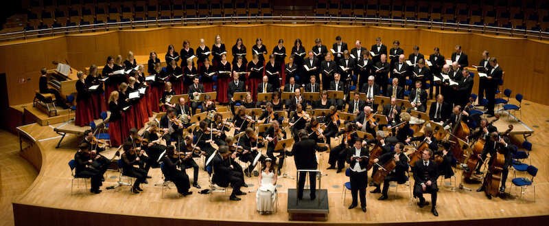 Ein Orchester und Chor auf einer Bühne in einem Konzertsaal, dirigiert von einer Person. Die Musiker spielen klassische Instrumente., © Musik Podium Stuttgart e.V. Ein Orchester und Chor auf einer Bühne in einem Konzertsaal, dirigiert von einer Person. Die Musiker spielen klassische Instrumente., © Musik Podium Stuttgart e.V.