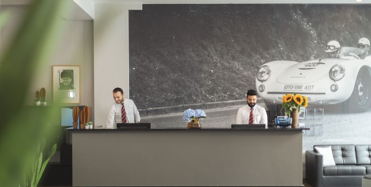 Zwei Männer an einer Hotelrezeption mit Blumen und einem großen Wandbild eines Rennwagens im Hintergrund., © Novum Hospitality