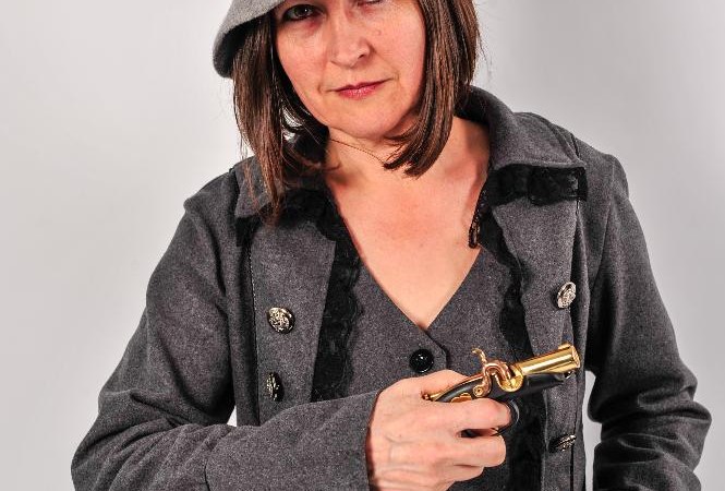 Eine Frau in einem grauen Mantel mit Kn&ouml;pfen und einem Filzhut h&auml;lt eine kleine Pistole in der Hand., &copy; Studio 1 Stuttgart