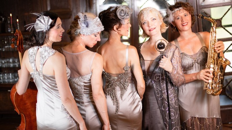 F&uuml;nf Frauen in eleganten, silbernen Kleidern der 1920er Jahre posieren mit Musikinstrumenten in einem stilvollen Raum. Sie verk&ouml;rpern den Glamour der Zeit., &copy; Touristik Bad Wildbad GmbH