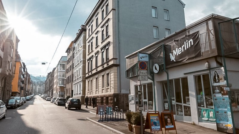 Stra&szlig;enszene in Stuttgart mit dem Kulturzentrum Merlin e.V. rechts im Bild. Die Sonne scheint, Autos parken entlang der Stra&szlig;e., &copy; Merlin, Stuttgart