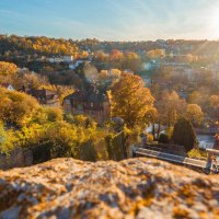 Herbstliche Landschaft in Schw&auml;bisch Hall mit buntem Laub und Sonnenstrahlen. Im Vordergrund ein Felsen, im Hintergrund H&auml;user und H&uuml;gel., &copy; Stadt Schw&auml;bisch Hall, Michael K&uuml;hneisen